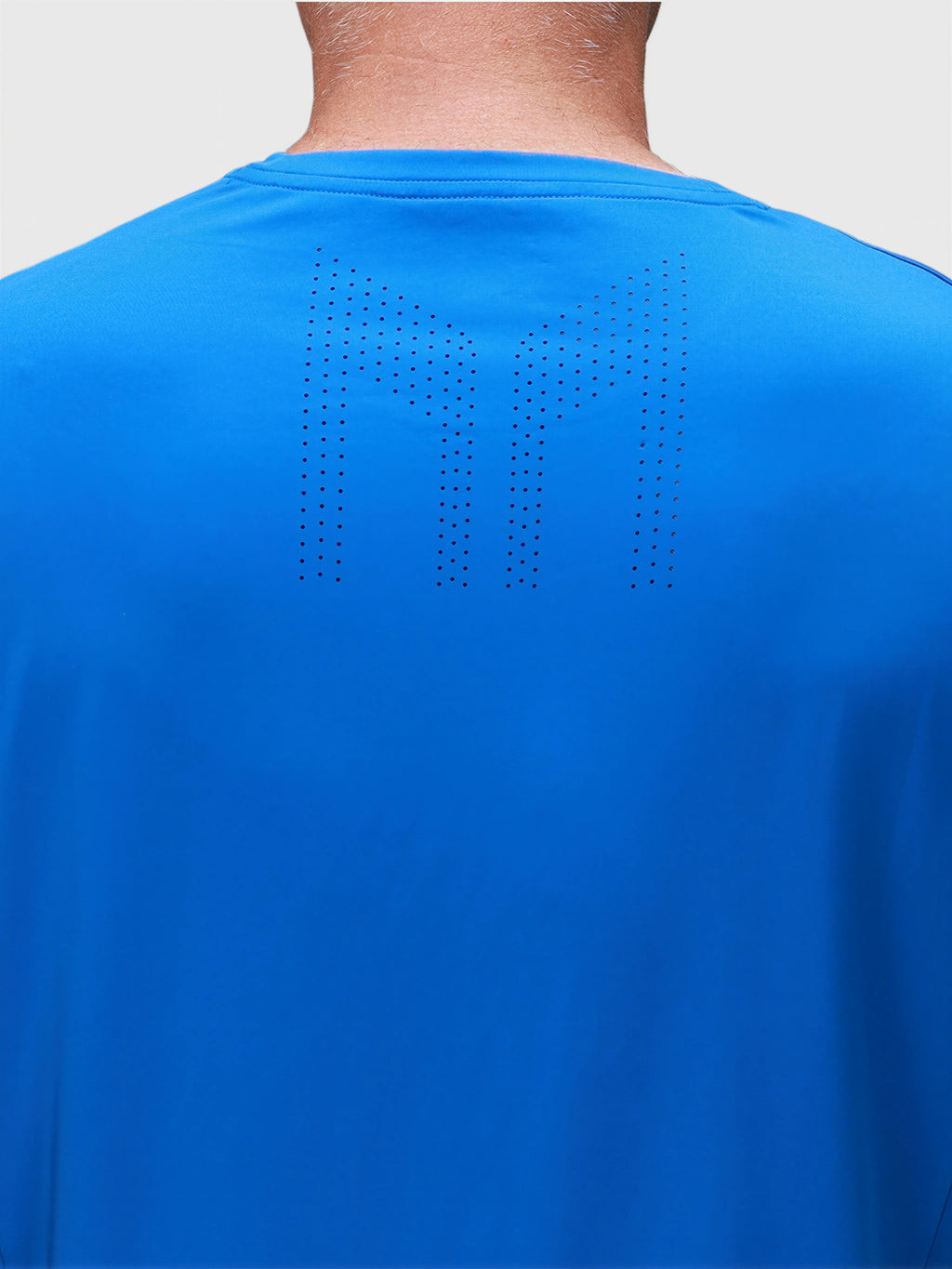 Rear view of person wearing bright blue Chevron Tee with perforated MUEV logo in padel apparel
